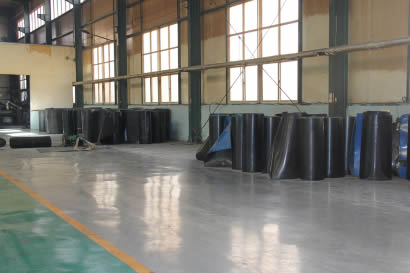 Many rolls of rubber sheet are on the floor of the workshop.