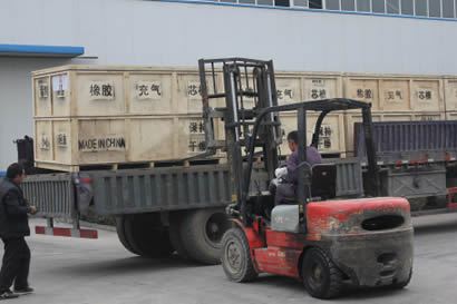 A person is lifting the wooden boxes to a truck with a forklift.